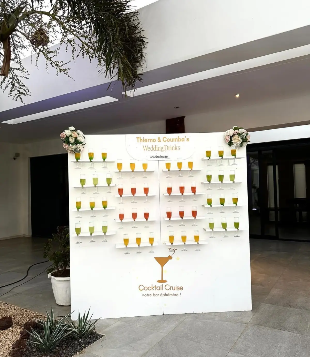 Mur de welcome drinks personnalisé pour un mariage, coupes colorées sur étagères blanches